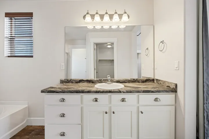 Vanity featuring white cabinetry, a single basin sink, and a dark patterned countertop