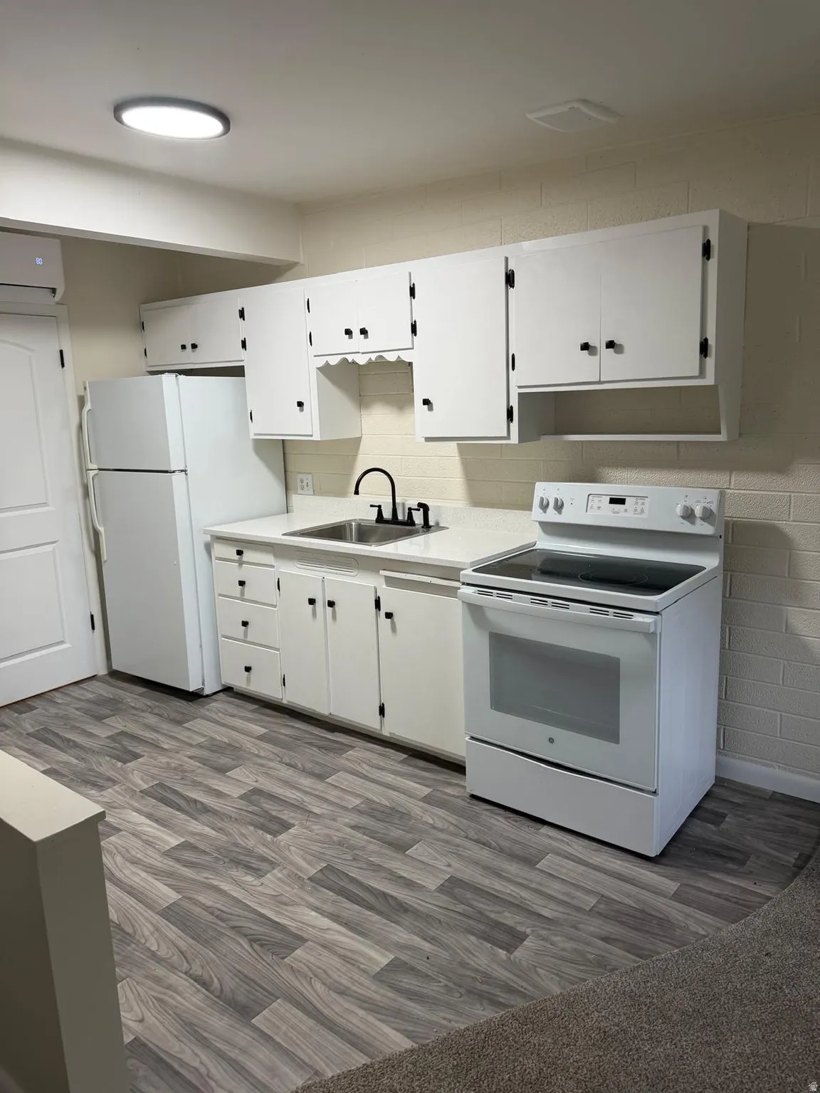 Kitchenette with white cabinetry, wood-finish flooring, white appliances, and a black gooseneck faucet