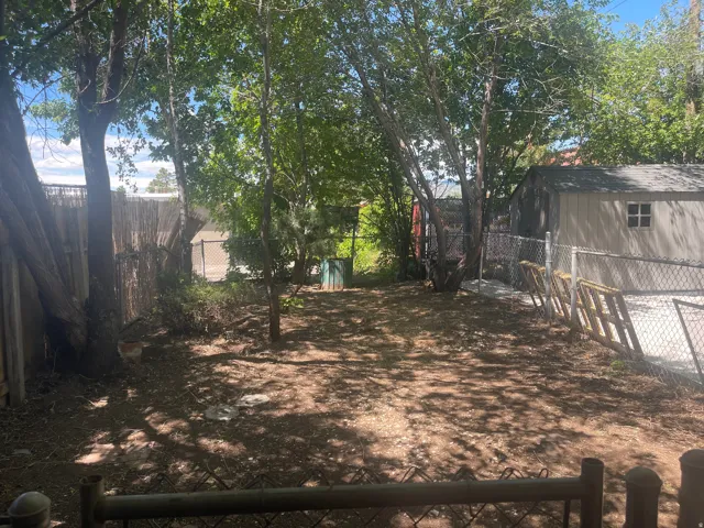 Spacious backyard featuring established trees, chain-link fencing, a wooden privacy fence, and a storage shed with a shingled roof and window