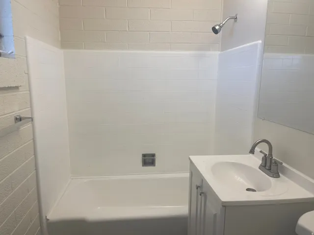 Bathroom featuring a white bathtub, white tiled shower surround, a chrome showerhead, a white vanity with an integrated sink, and a chrome faucet