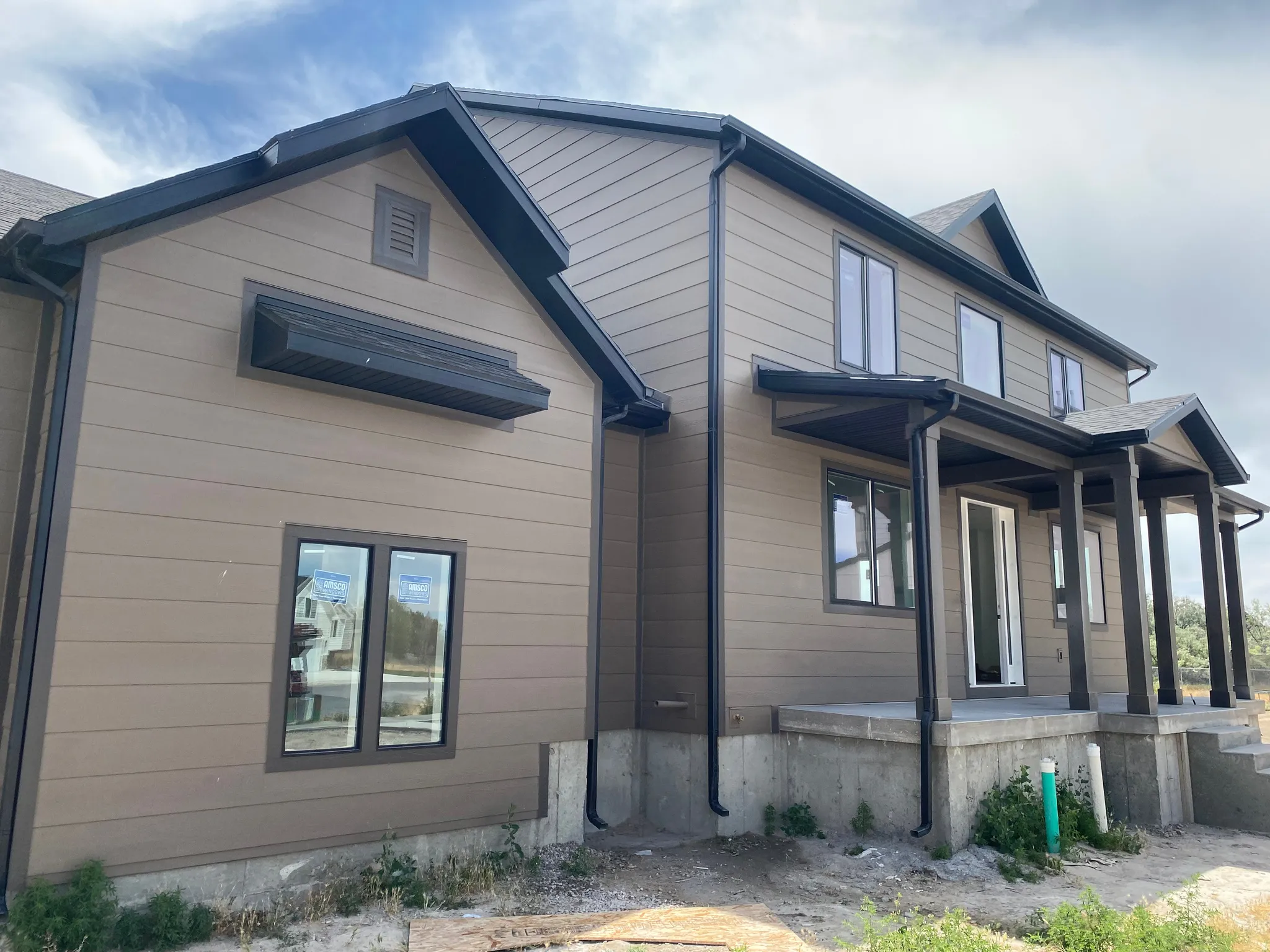 Exterior featuring horizontal siding with dark trim, multiple windows with dark frames, a covered front porch with dark columns, and dark-finished gutters