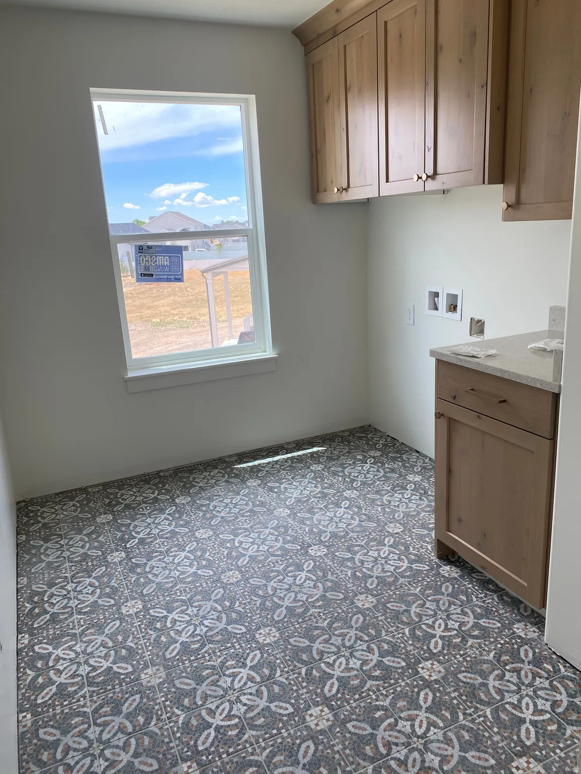 Laundry room featuring patterned tile flooring, light wood-finish cabinetry, a single window, and a light-toned countertop