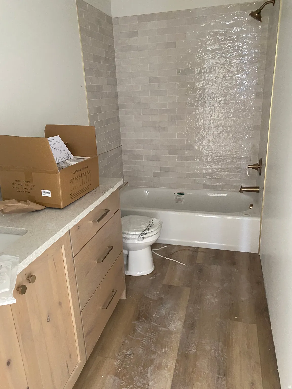 Bathroom featuring wood-finish flooring, a white bathtub with light gray subway tile surround, and bronze fixtures