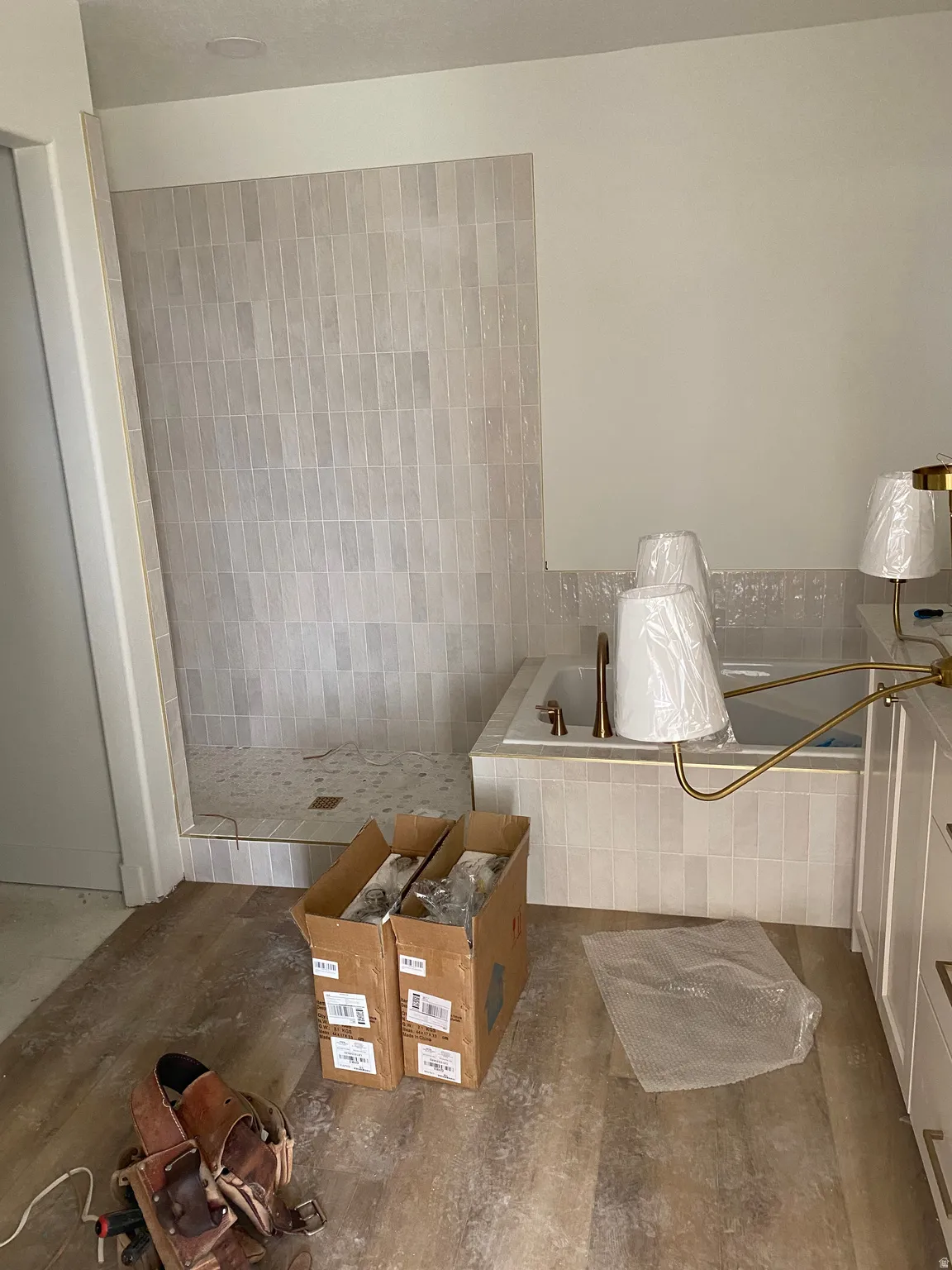 Bathroom featuring a walk-in shower with vertical subway tile, a built-in tub with coordinating tile surround, and an adjacent vanity with white cabinetry and gold-tone hardware
