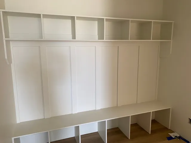 Built-in white storage bench with open shelving, wall paneling, and wood-finish flooring