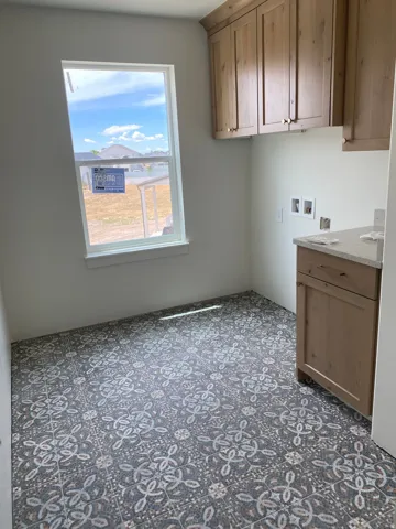 Laundry room featuring patterned tile flooring, light wood-finish cabinetry, a single window, and a light-toned countertop
