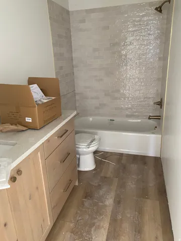 Bathroom featuring wood-finish flooring, a white bathtub with light gray subway tile surround, and bronze fixtures