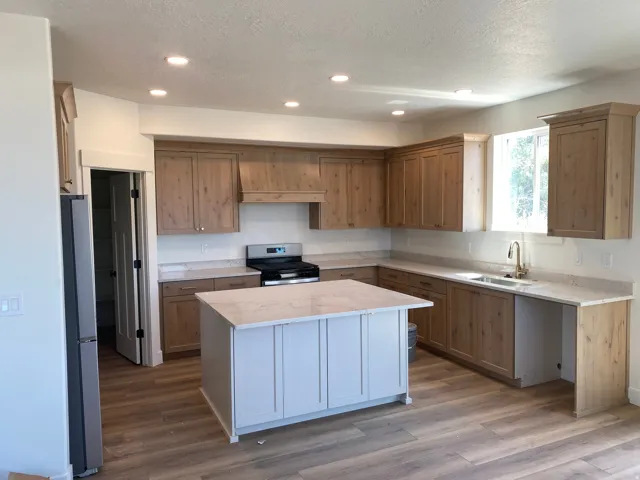Newly constructed kitchen featuring custom wood cabinetry, light wood-finish flooring, and a large center island with light blue painted base and wood countertop