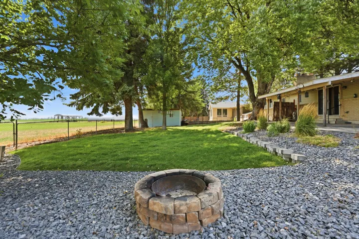 Expansive backyard featuring a stone-ringed fire pit, gravel landscaping, and a manicured lawn