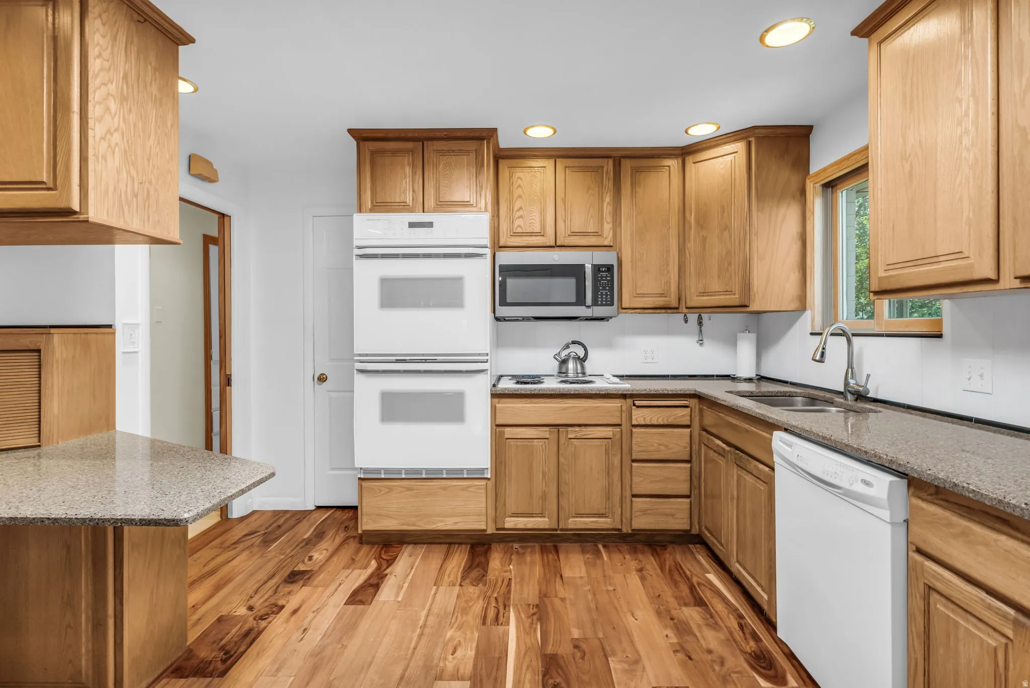 Kitchen featuring wood-finish flooring, recessed lighting, double wall ovens, a built-in microwave, and ample wood cabinetry