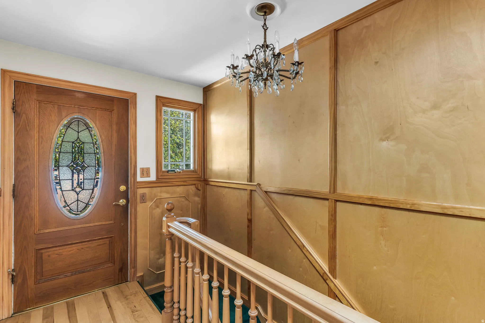 Entryway featuring a wood-panel accent wall, a chandelier with crystal elements, and a wood-finish door with an oval leaded glass insert