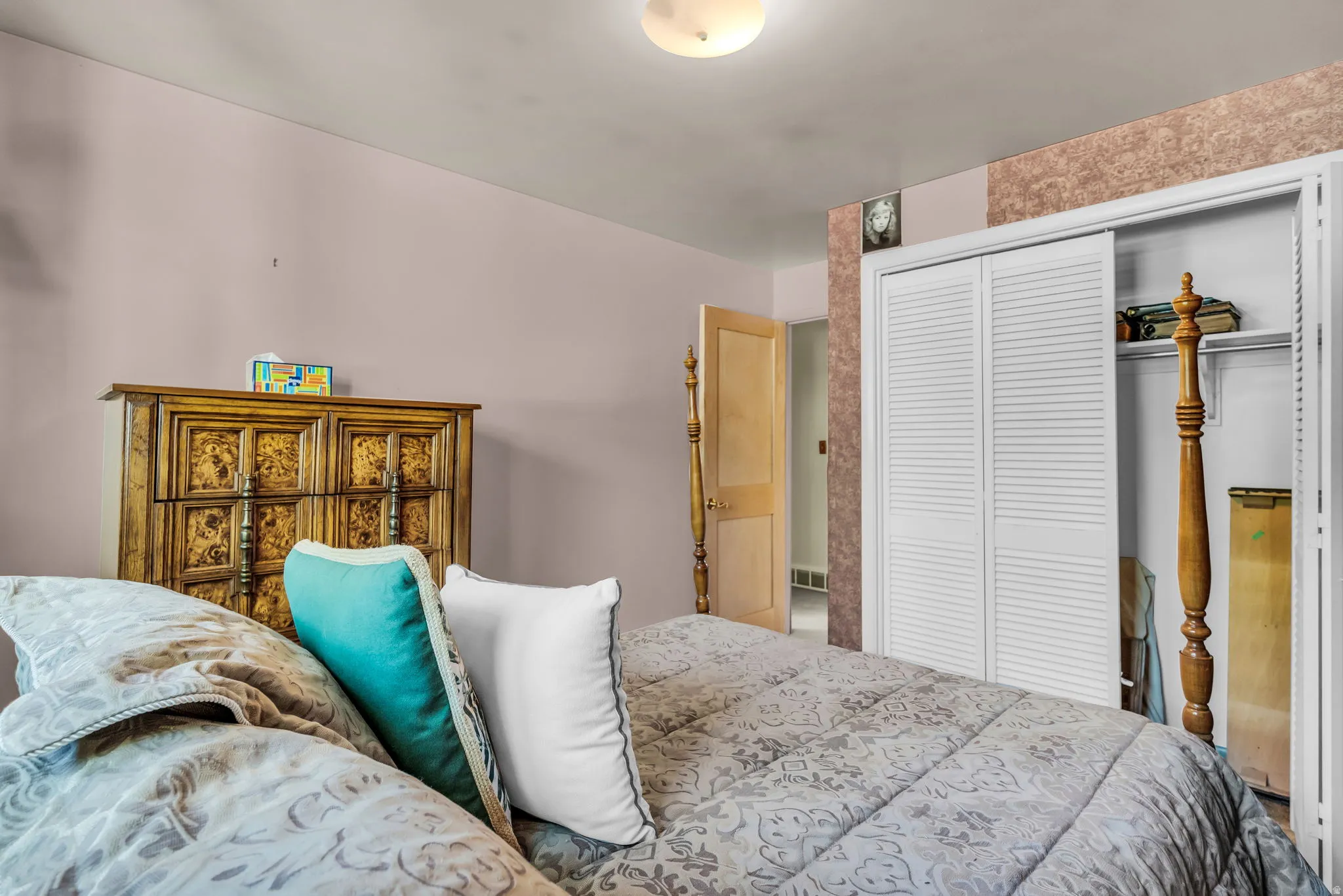 Bedroom featuring light pink walls, white louvered bifold closet doors, and an overhead flush-mount light fixture