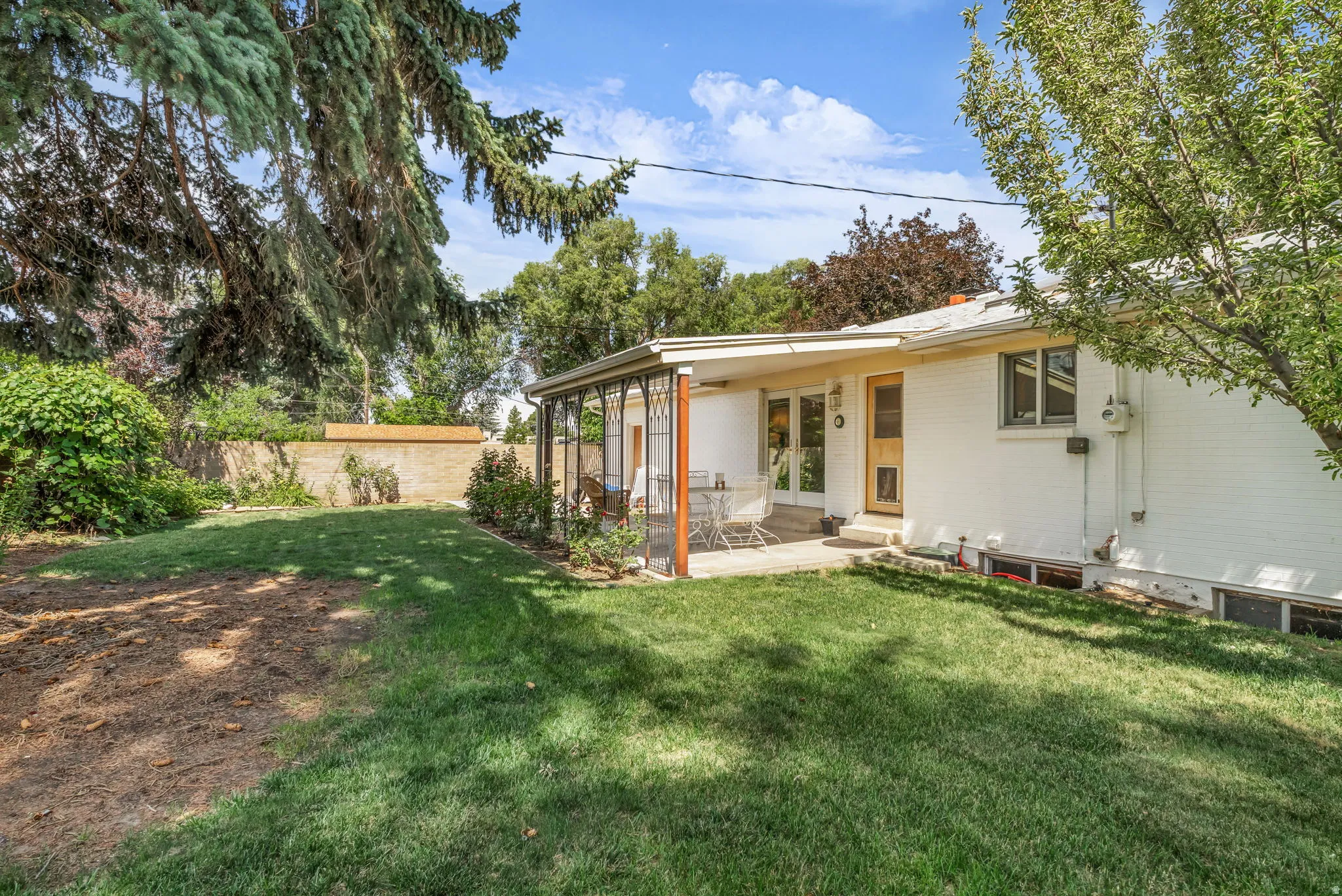 Expansive backyard featuring a covered patio, mature trees, and a white brick exterior