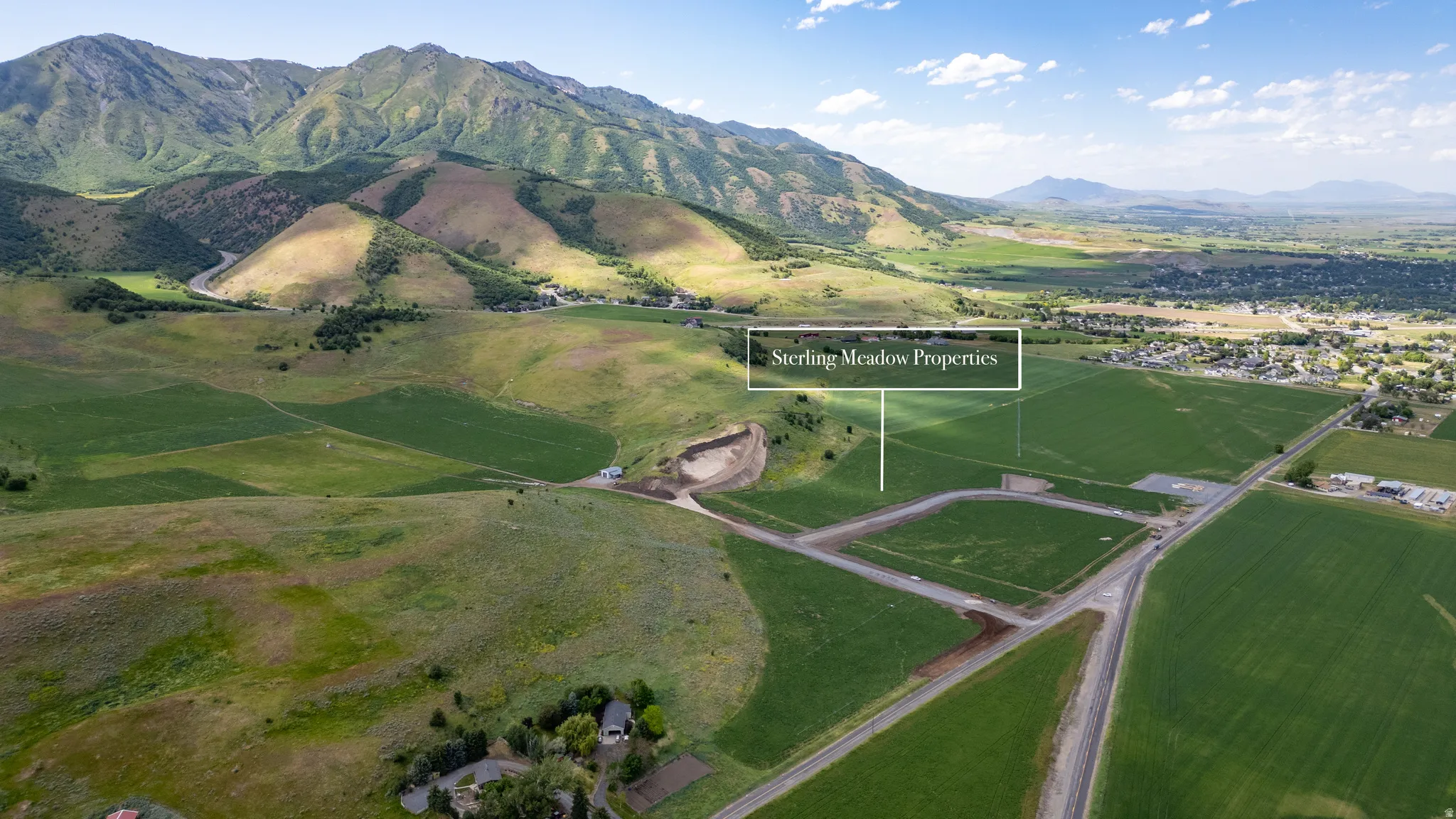 Expansive undeveloped land featuring a mountainous backdrop, green fields, and visible road infrastructure