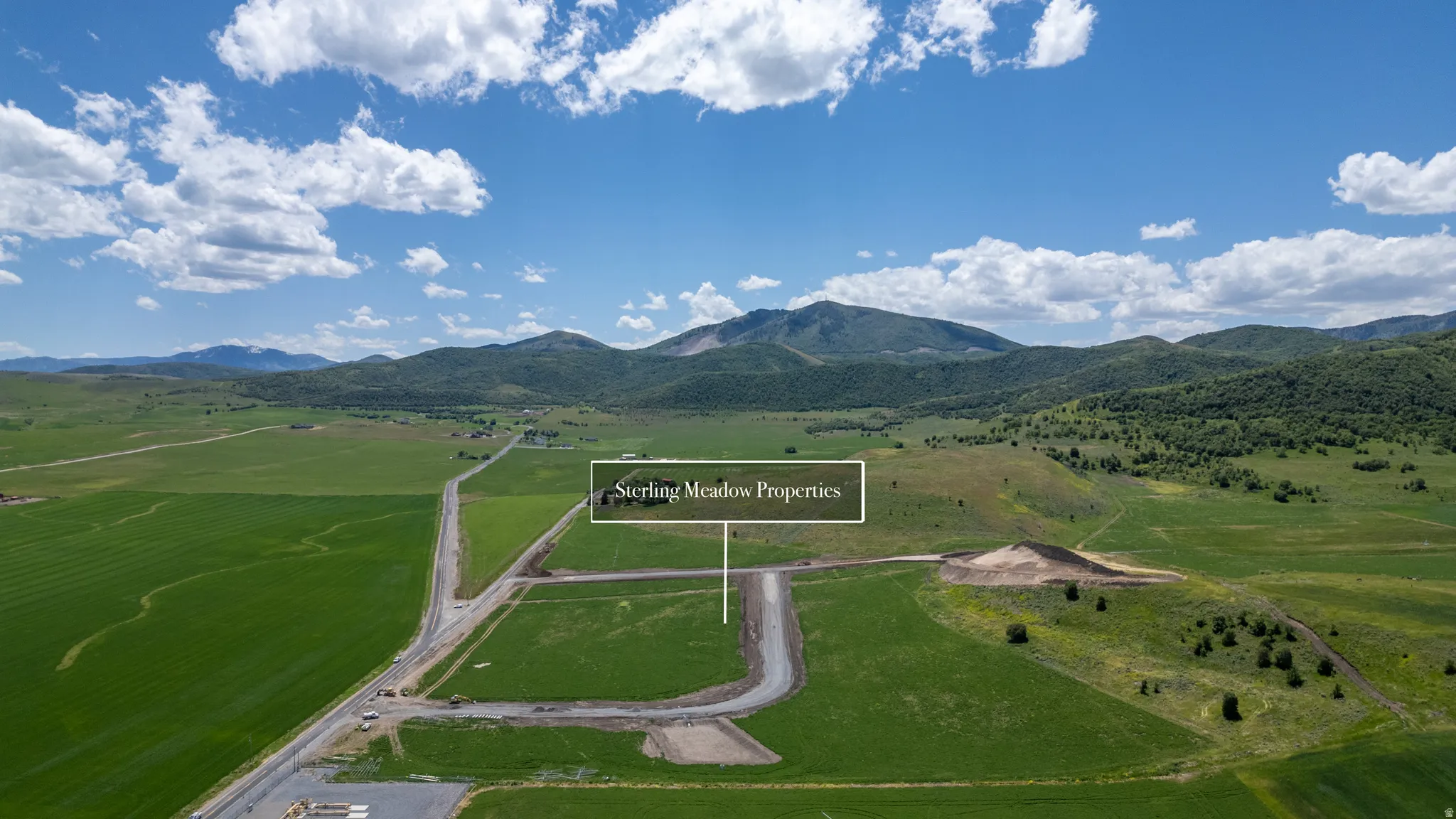 Expansive undeveloped land featuring a paved road, green fields, and distant mountain ranges