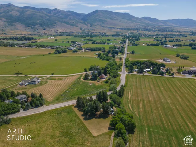 Expansive rural landscape featuring a paved road, scattered residential properties, mature trees, open fields, and distant mountains