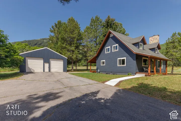 Modern farmhouse-style home with dark blue siding, a stone chimney, and a covered front porch with exposed wood beams