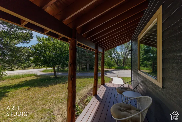 Covered front porch featuring natural wood beams and decking, dark horizontal siding, a light-trimmed window, and a concrete walkway extending to the foreground
