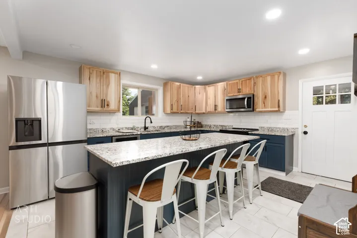 Kitchen featuring a large island with a granite countertop, shaker-style base cabinetry in a deep blue finish, natural wood-finish upper cabinetry, and a white subway tile backsplash