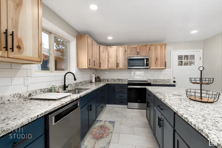 Contemporary kitchen featuring two-tone cabinetry with natural wood-finish upper cabinets and matte blue lower cabinets, granite countertops, subway tile backsplash, and stainless steel appliances