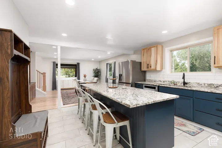 Bright kitchen featuring an expansive center island with granite countertops, blue shaker-style cabinetry, stainless steel appliances, and wood-finish flooring