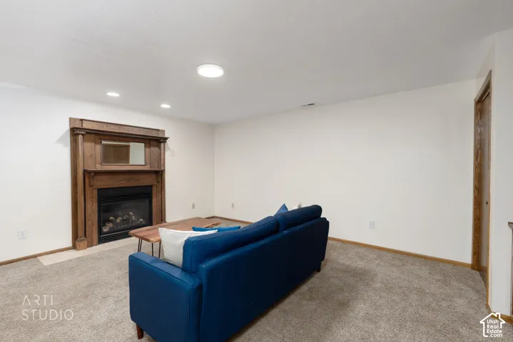 Living space featuring a detailed wood fireplace surround with an integrated mirror, recessed ceiling lighting, and neutral carpet flooring