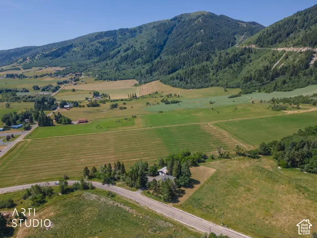 Expansive property featuring verdant fields, a primary residence with an attached garage, a paved road frontage, and a backdrop of verdant mountains