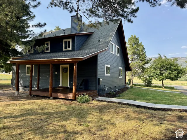 Two-story residence featuring dark siding, a covered front porch with natural wood posts, and a prominent chimney