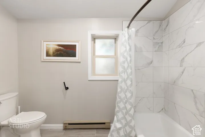 Bathroom featuring a white porcelain toilet, white window trim, white subway tile shower surround with gray veining, and gray tile flooring