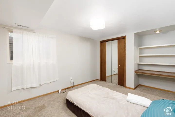 Carpeted room featuring a window, built-in shelving with an integrated desk surface, a mirrored closet with wood-finish sliding doors, and a flush-mount ceiling light fixture