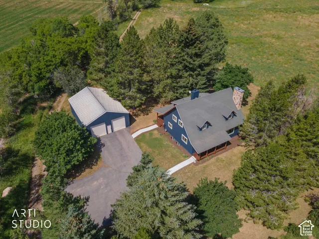 Expansive property featuring a blue-sided residence with a dark shingle roof and stone chimney, complemented by a detached two-car garage with a light-colored roof