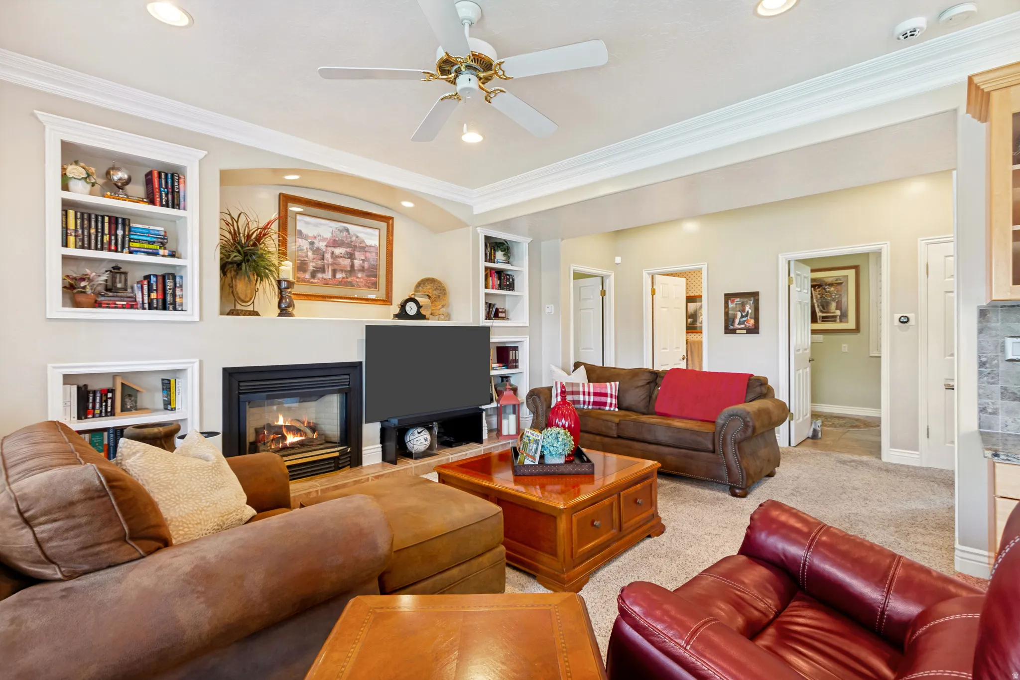 Spacious living area featuring a central fireplace with brick hearth, built-in shelving, recessed lighting, and a ceiling fan