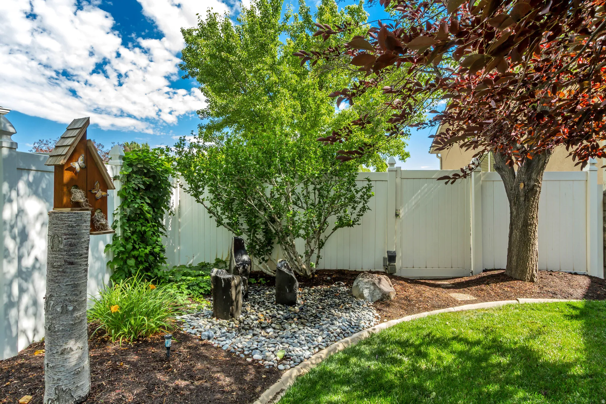 Manicured lawn area with a white privacy fence, mature trees, and decorative rock landscaping