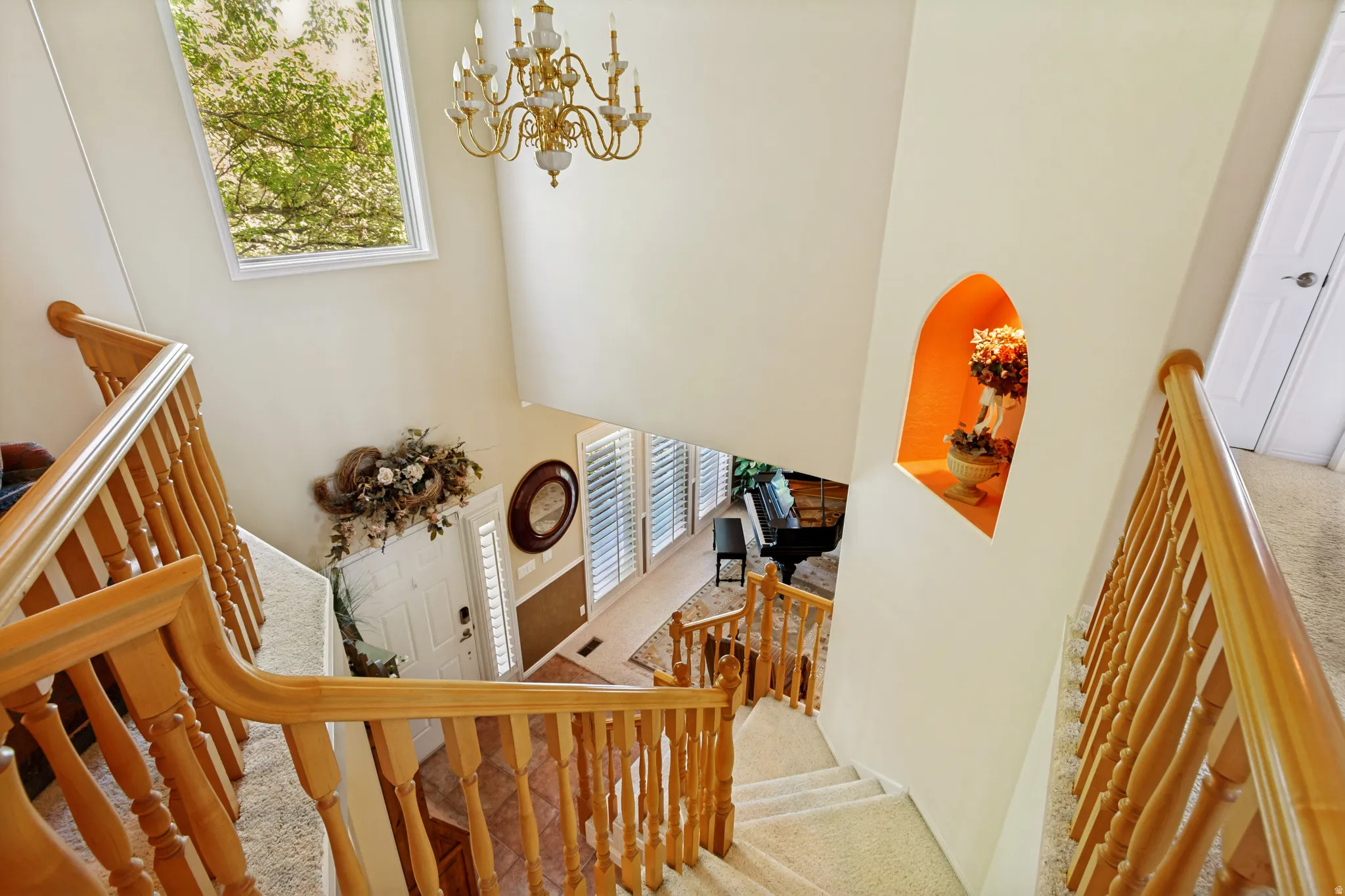 Grand entryway with a two-story ceiling, natural wood staircase and banister, arched wall niche, and an overhead chandelier