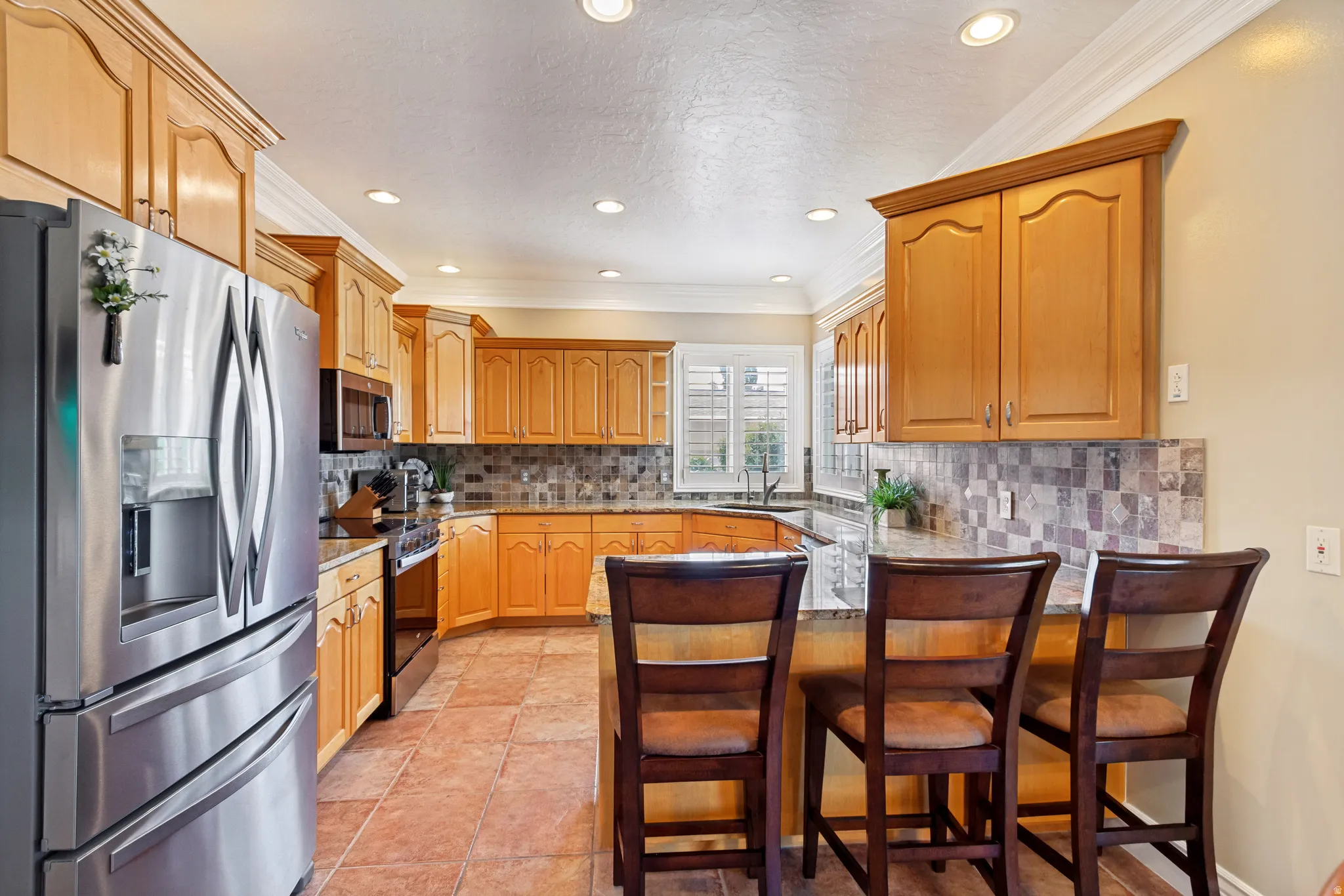 Kitchen featuring a stainless steel French door refrigerator, wood cabinetry, stone countertops, and a tiled backsplash