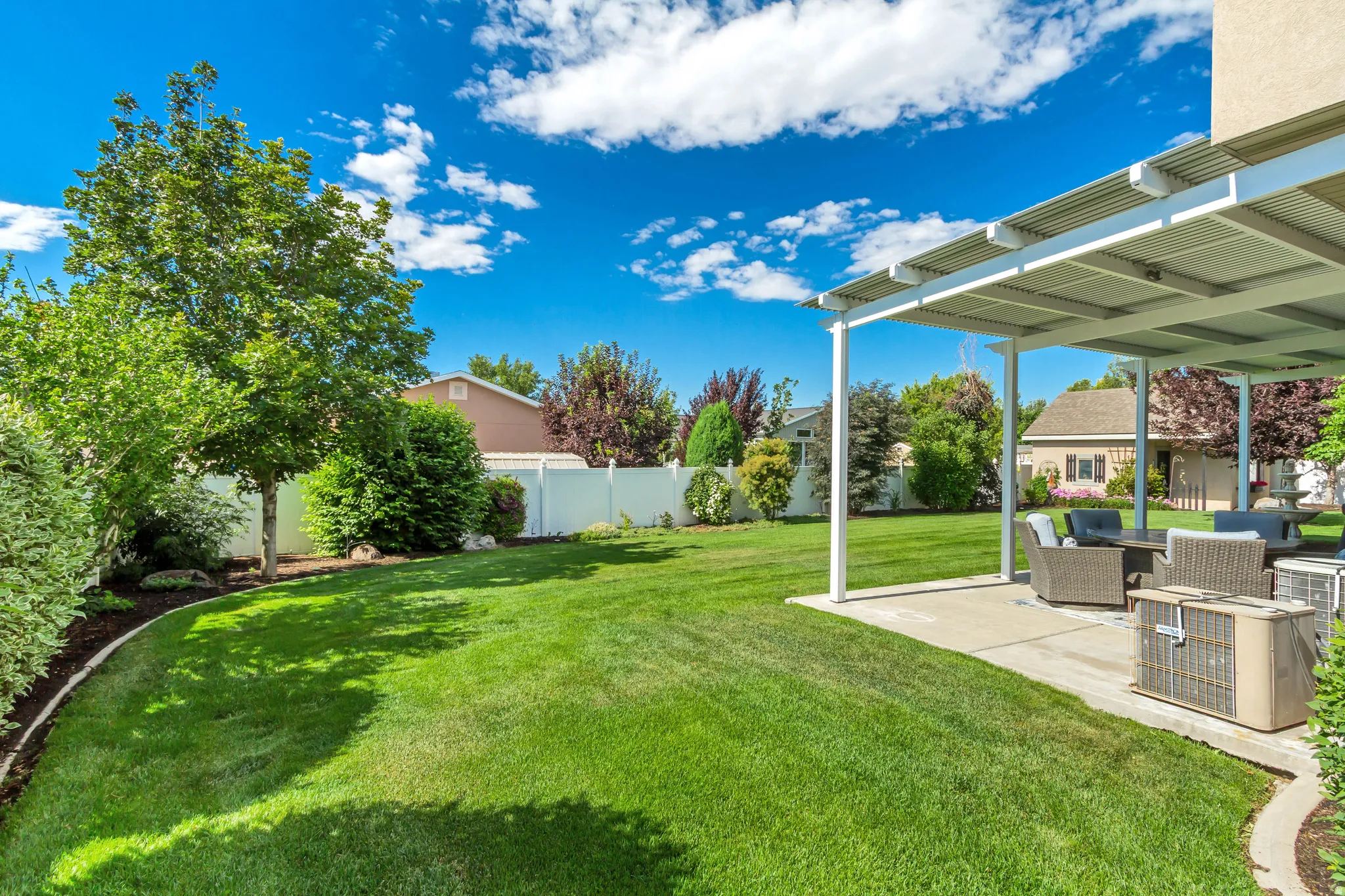 Expansive backyard featuring a large green lawn, mature trees, and a white privacy fence