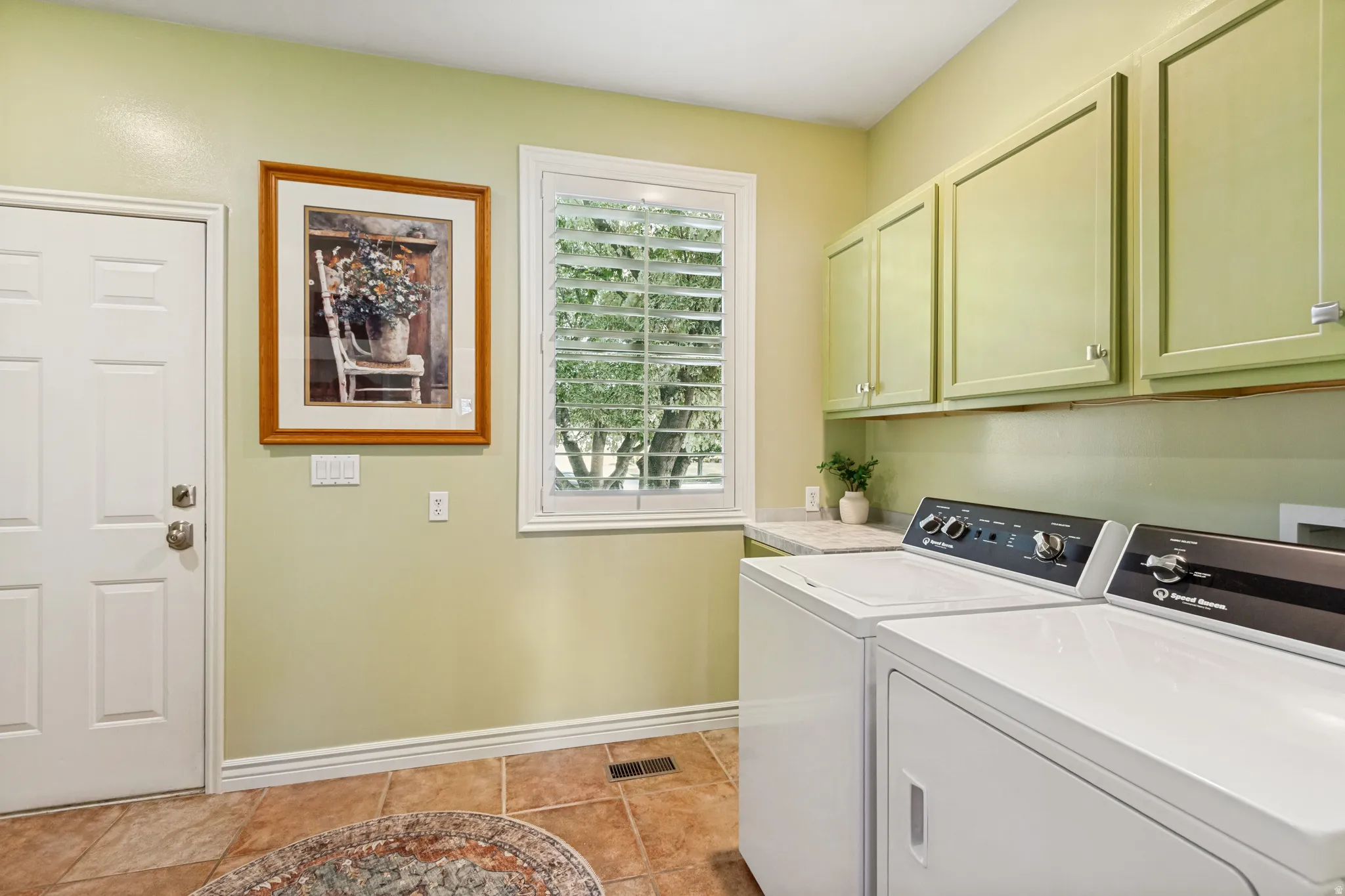 Laundry area featuring overhead cabinetry, a white paneled door, and a window with plantation shutters