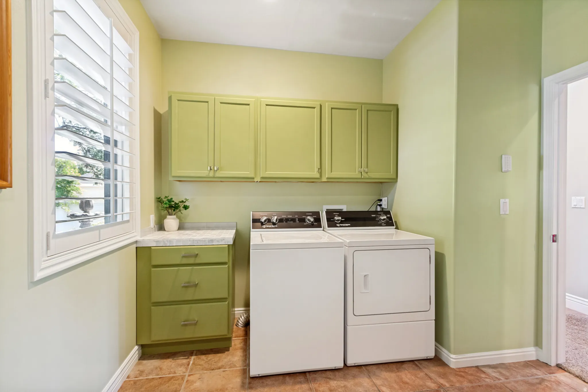 Laundry room featuring tile flooring, a window with plantation shutters, custom cabinetry, a countertop, and a built-in appliance space