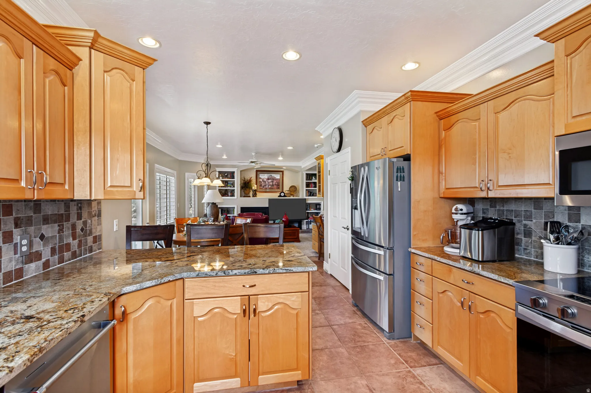 Spacious kitchen featuring light wood cabinetry, granite countertops, tile flooring, a mosaic tile backsplash, and stainless steel appliances