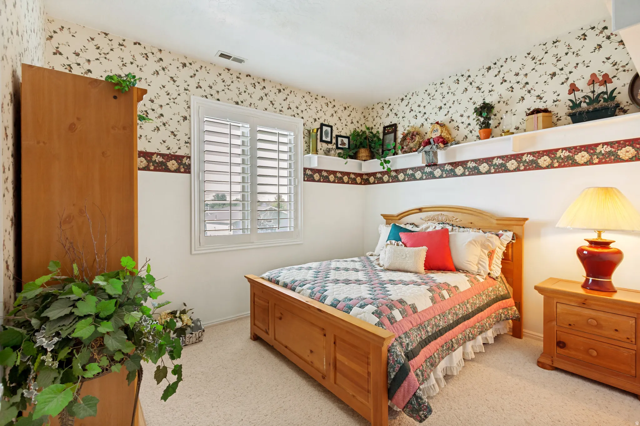 Bedroom featuring a window with white louvered shutters, wall shelving, and patterned wallpaper