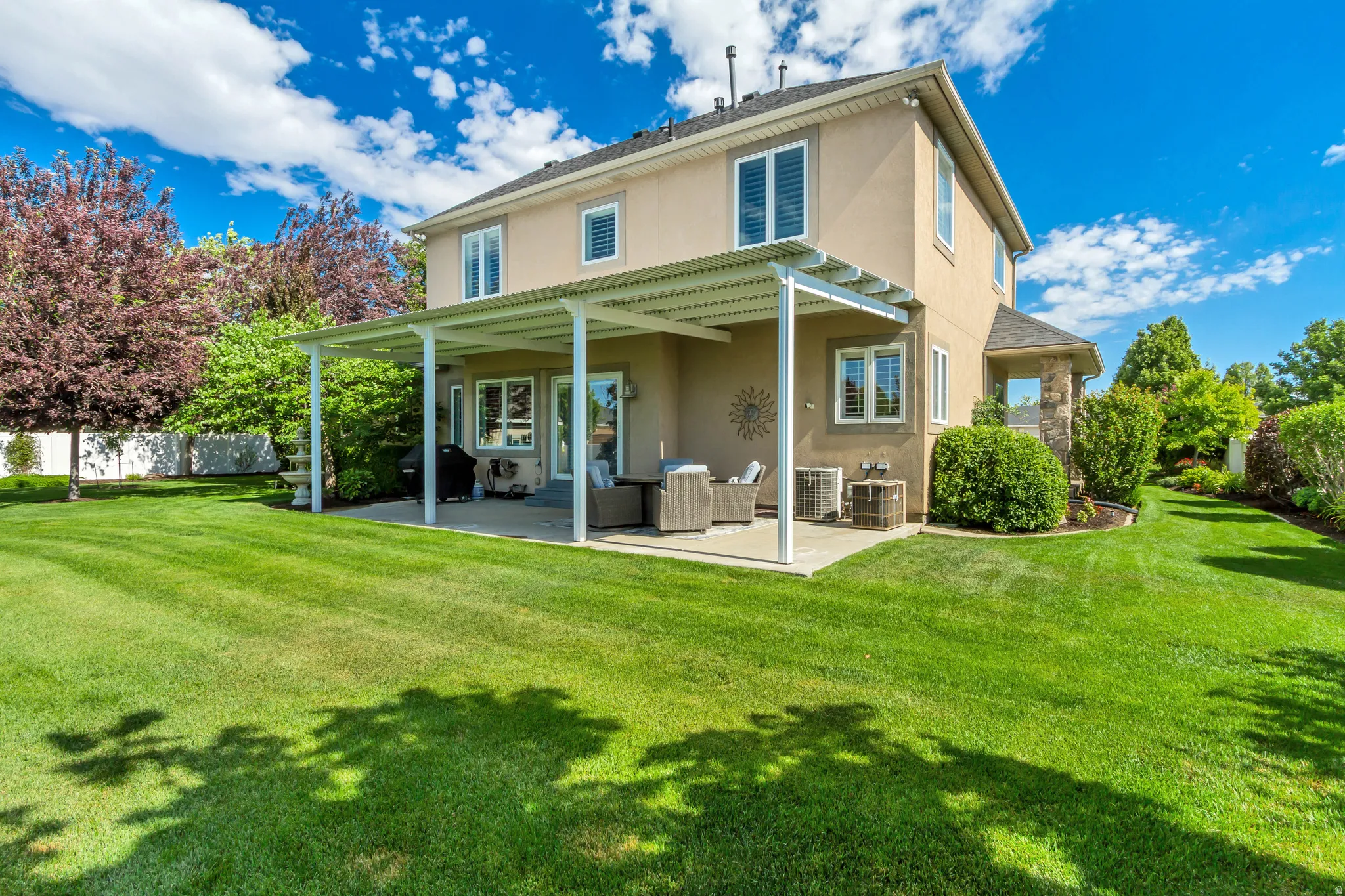 Expansive rear yard featuring a large concrete patio with a white metal pergola