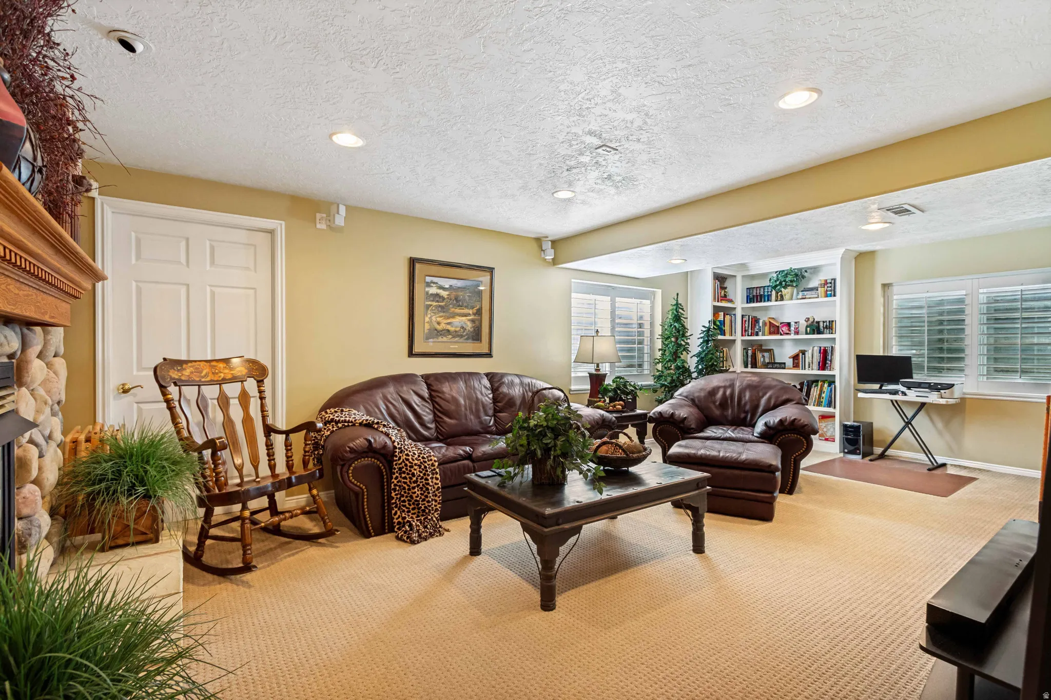Spacious living area featuring a stone fireplace with a wood mantel, built-in shelving, recessed lighting, and neutral carpeting