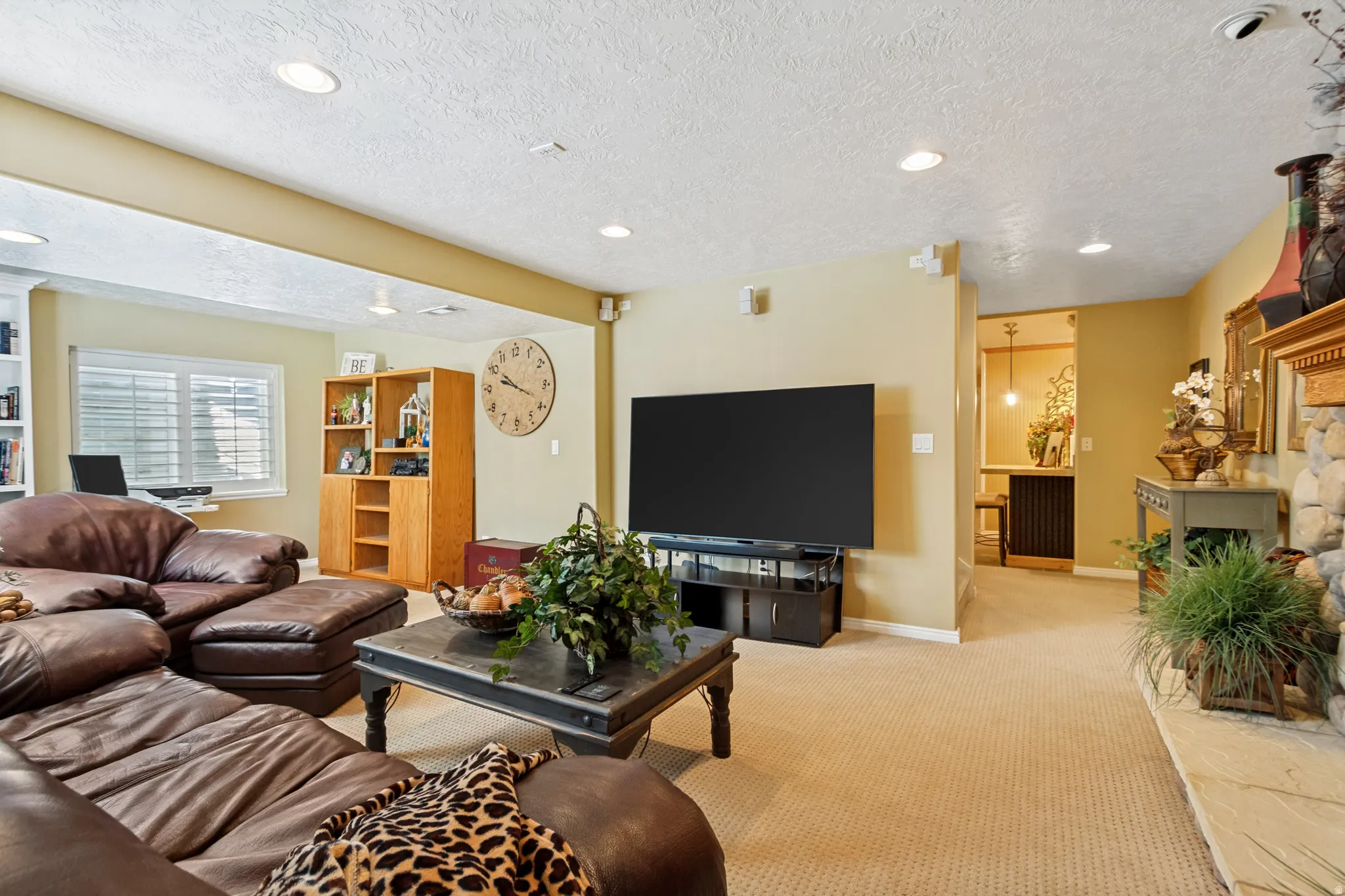 Spacious living area featuring recessed lighting, light tan carpeting, and a stone fireplace with a wood-finish mantel