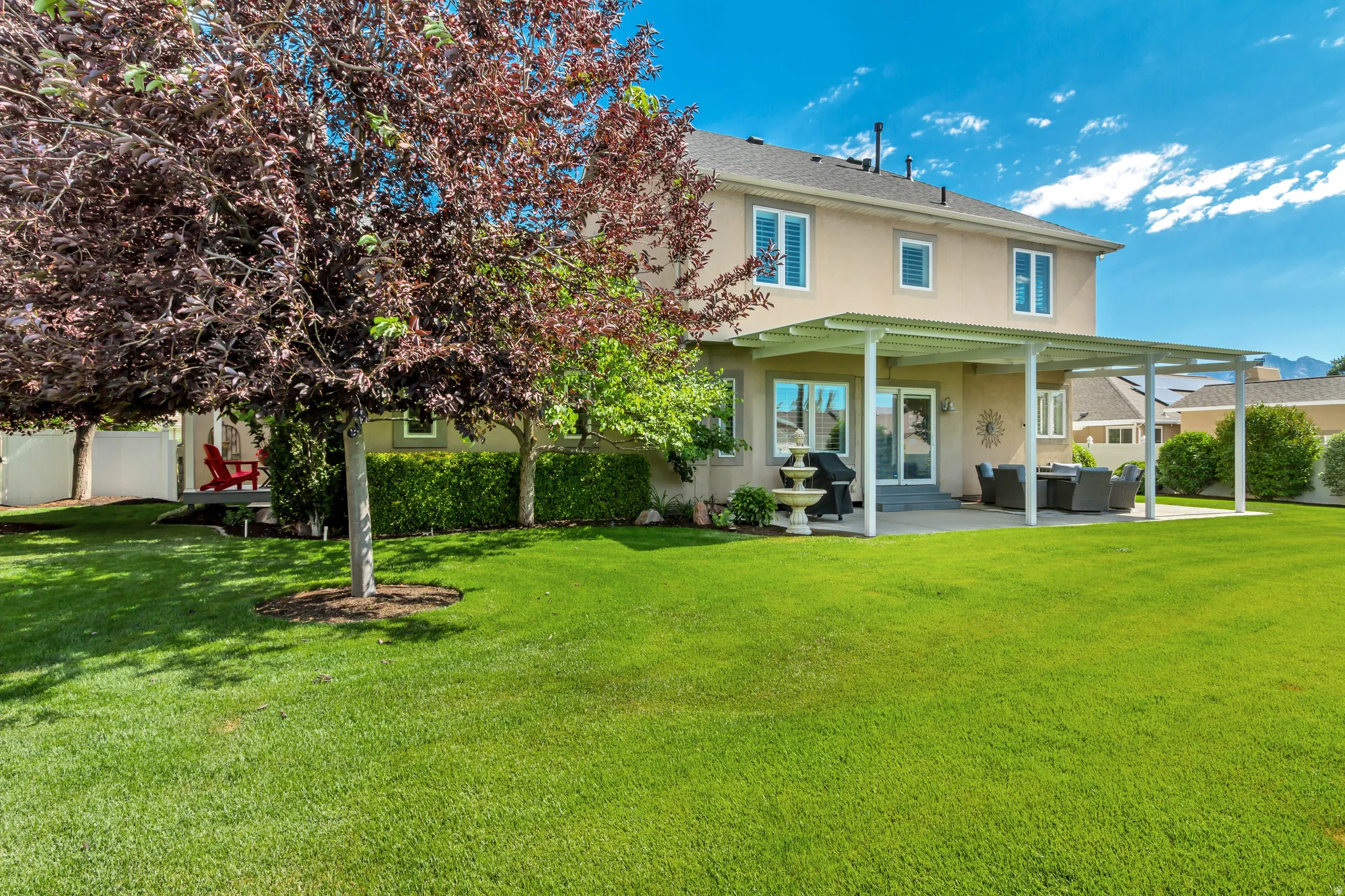 Expansive backyard featuring a large green lawn, mature trees, a covered patio structure, and a concrete patio