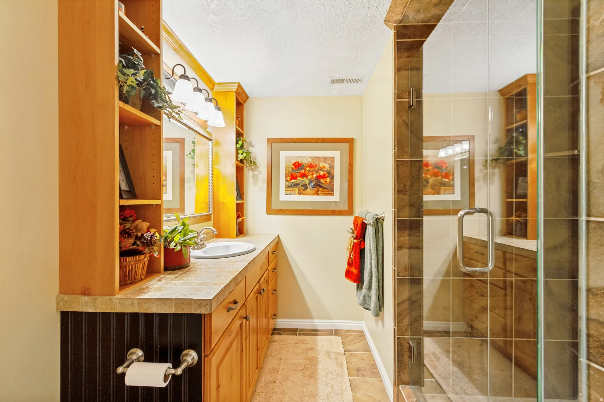Bathroom featuring a glass-enclosed shower with tile surround, a single vanity with an integrated sink, and wood-finish cabinetry