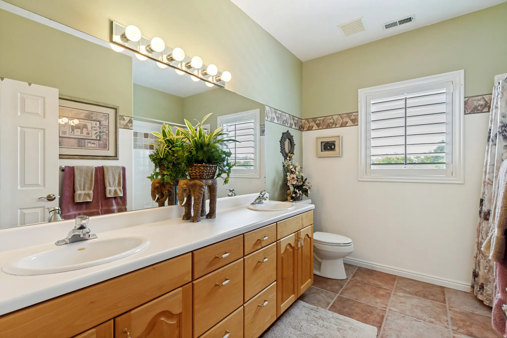 Bathroom featuring a dual vanity with light wood cabinetry, white countertops, and integrated sinks