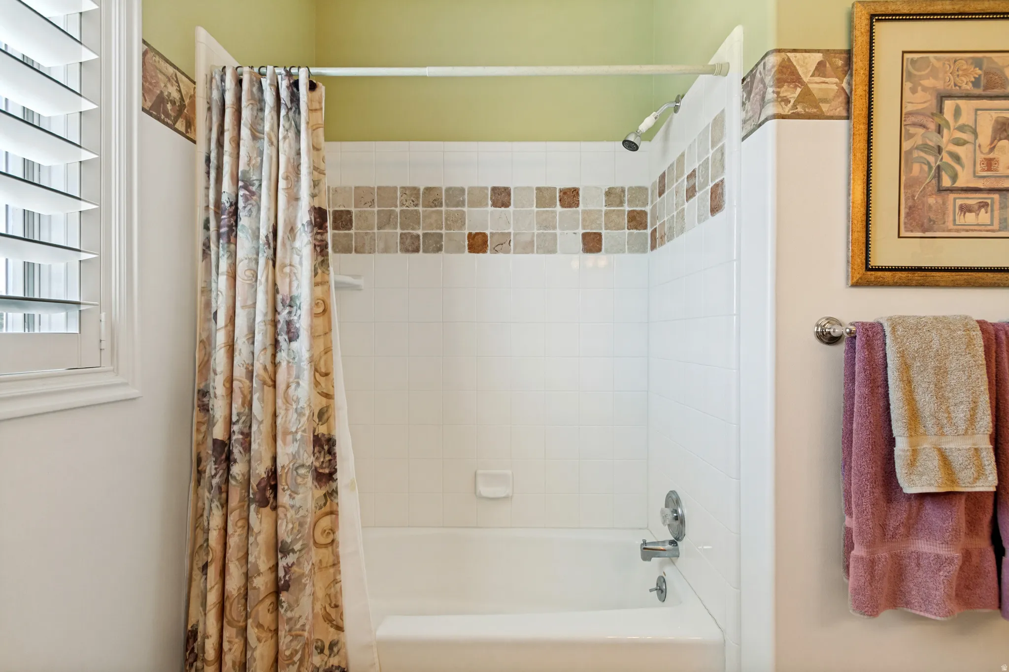 Bathtub with a tiled surround featuring a decorative mosaic border
