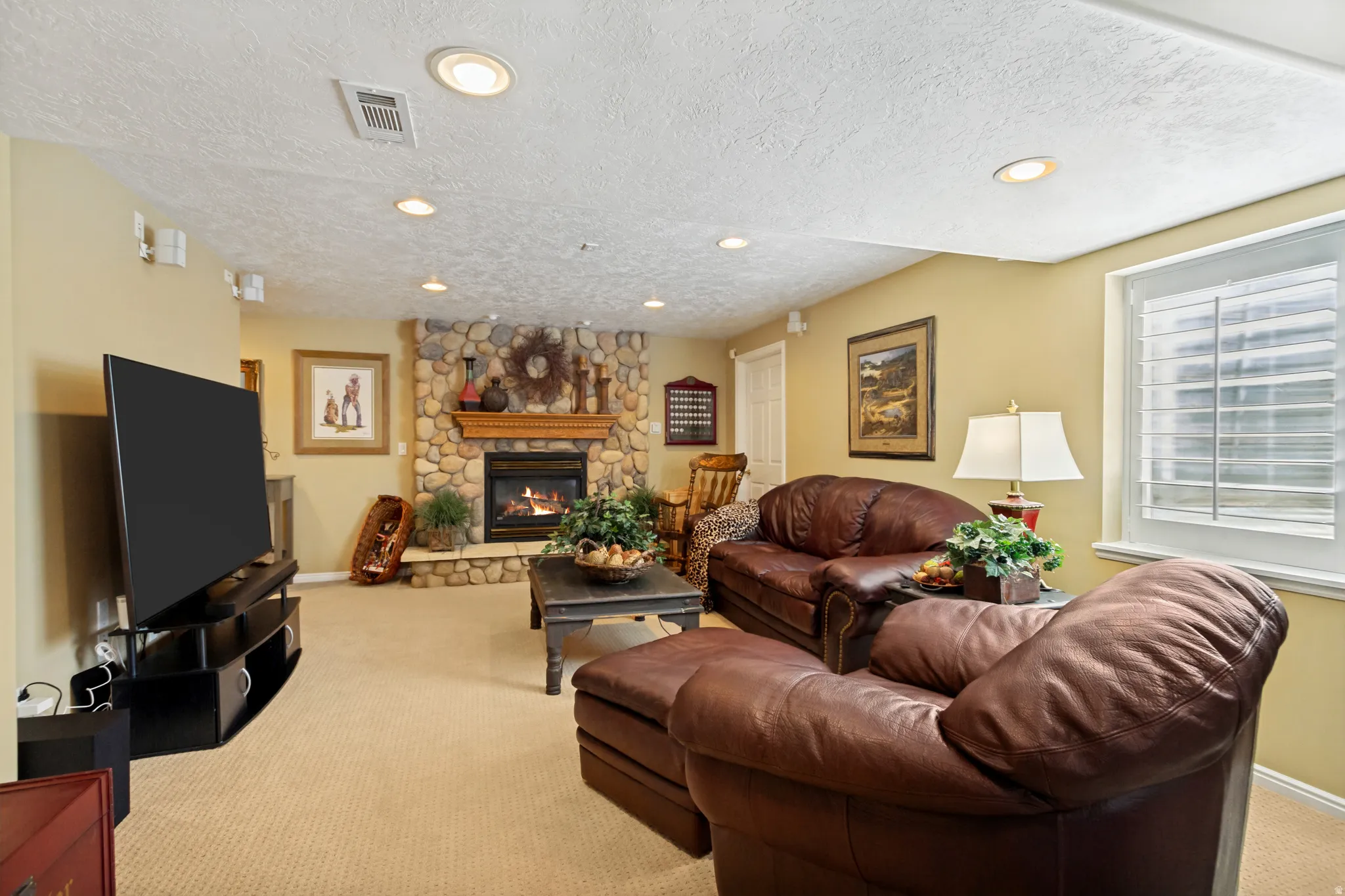 Living area featuring a stone-clad fireplace with a wood mantel, recessed lighting, and a window with white louvered blinds