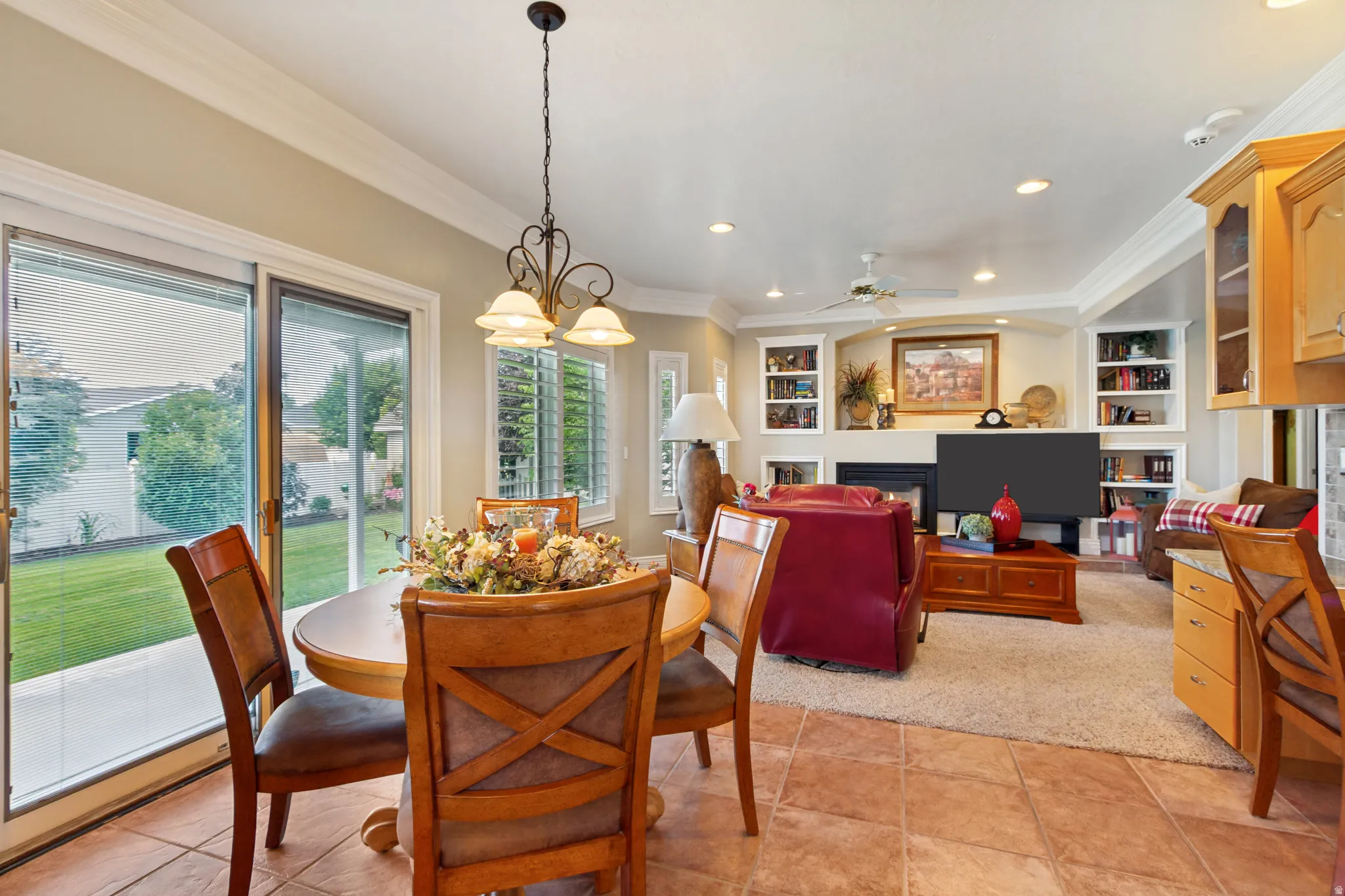 Open-concept living space featuring ceramic tile flooring, a fireplace with a mantel, built-in shelving, and crown molding