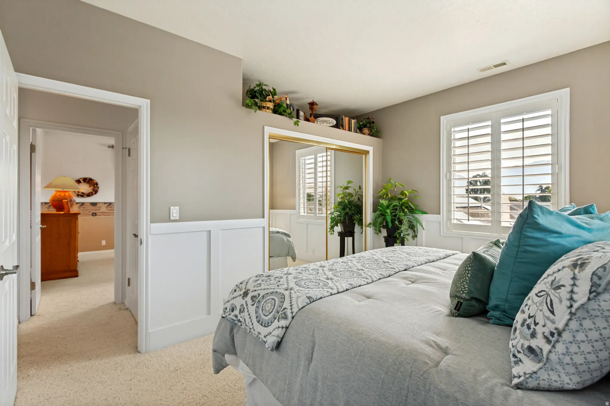 Carpeted room featuring white wainscoting, a gold-framed mirrored closet, and a window with white plantation shutters